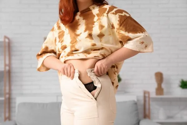 Image of woman trying to do her trousers up after pregnancy weight gain Wisley