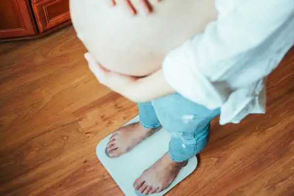 Image of woman weighing herself and experiencing weight gain through pregnancy Wisley